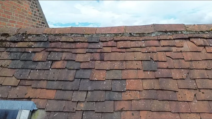 Older clay tiled roof with slipped and uneven tiles and deteriorated ridge bedding