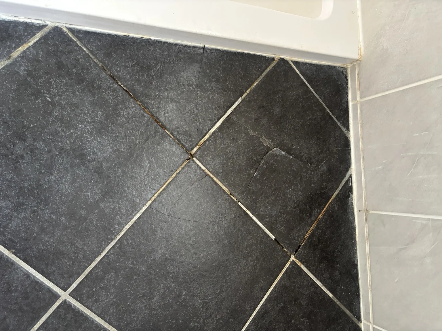 Cracked bathroom floor tiles and damaged grout revealed beneath a bath mat
