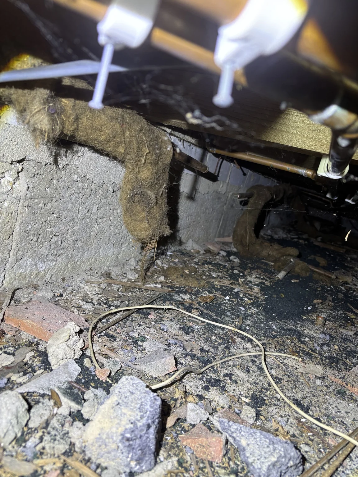 Older fibrous lagging around redundant-looking pipework beneath a suspended timber floor